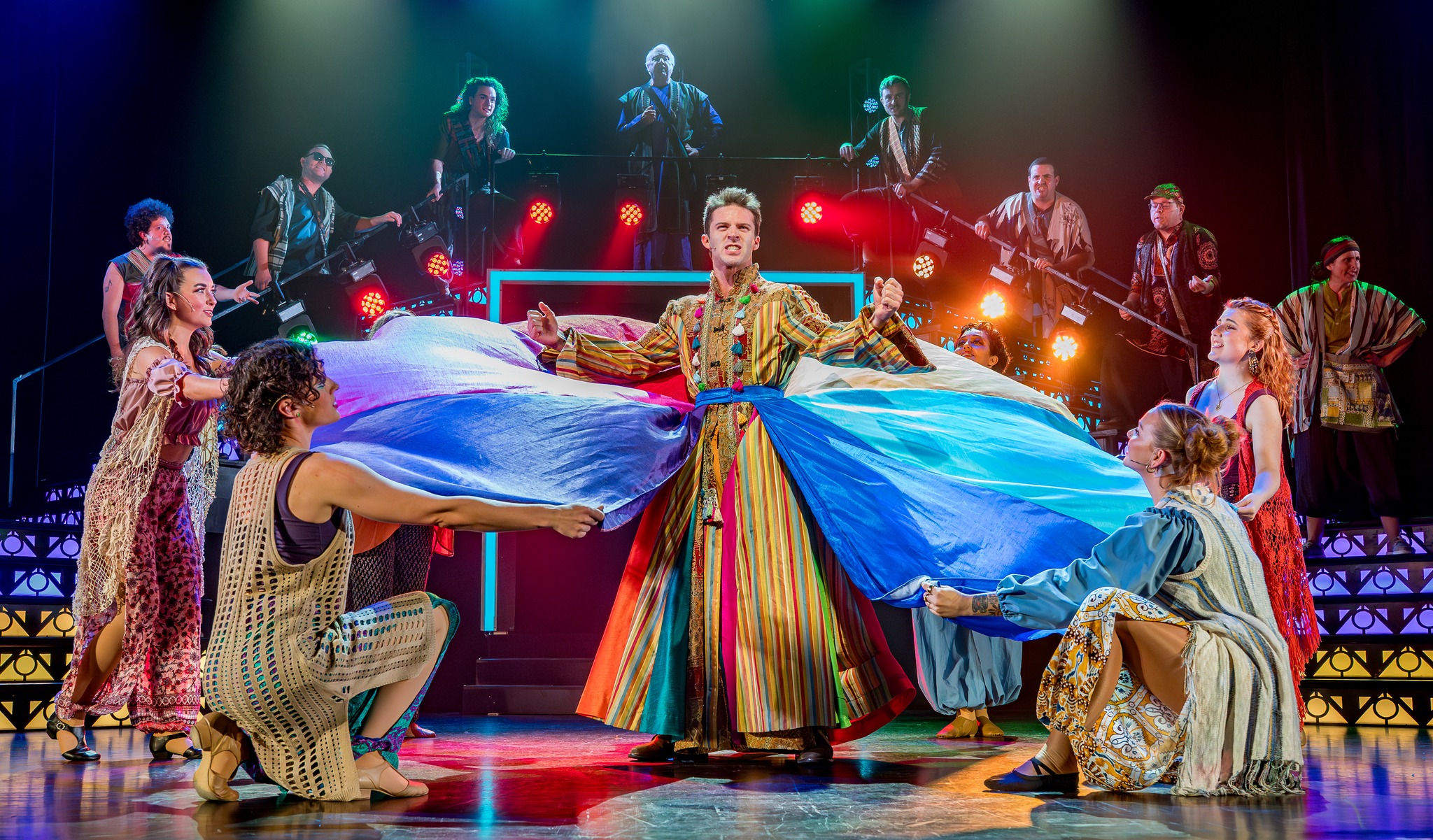 A performer in a colorful striped coat on stage under red lights